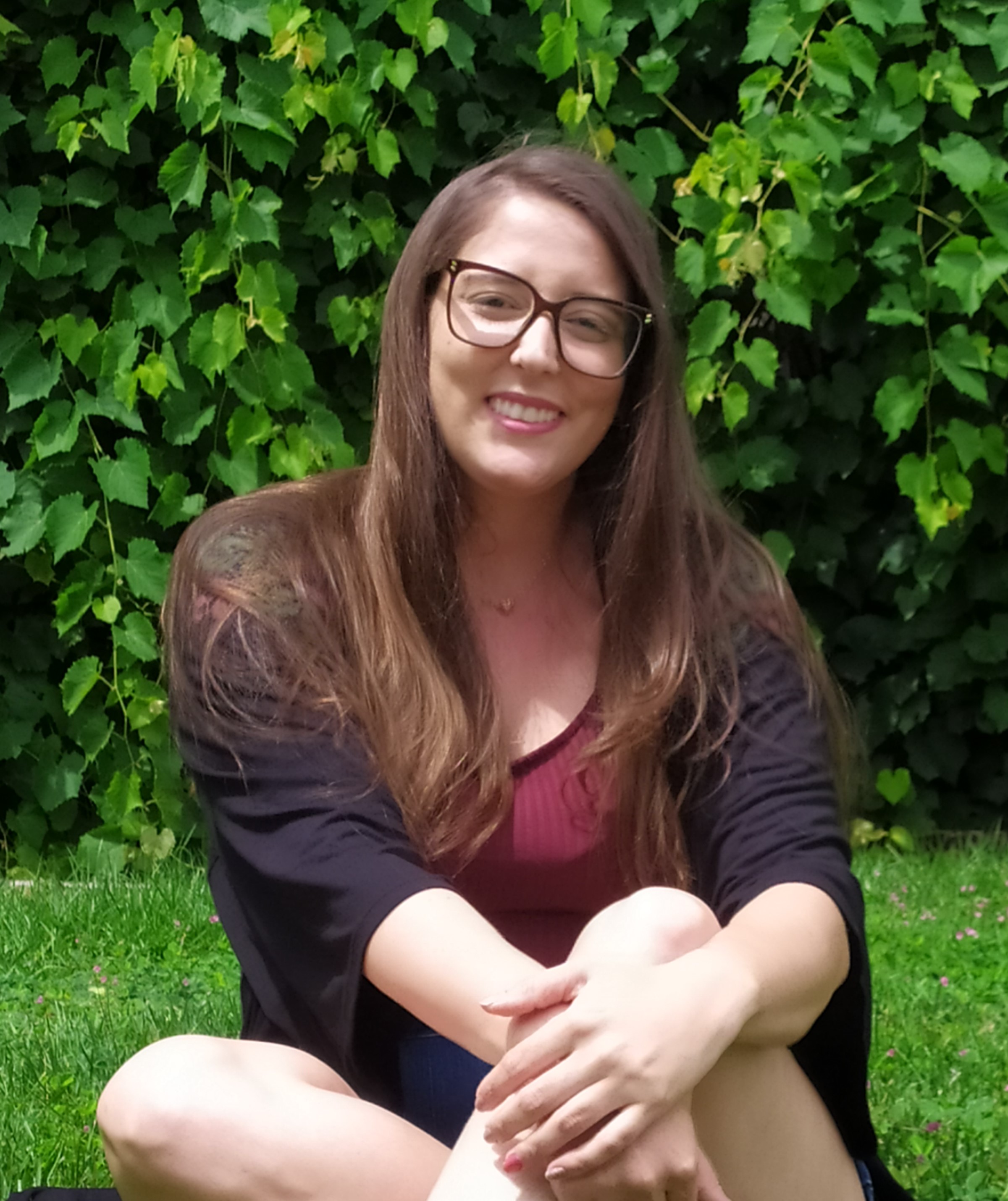 mulher caucasiana, de óculos, cabelos compridos, ao fundo folhas verdes